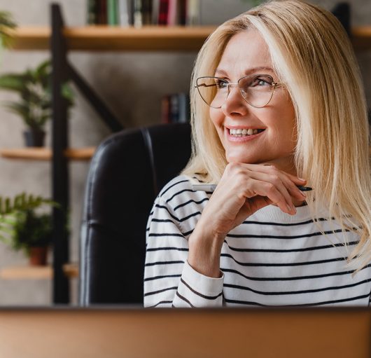 happy-senior-woman-holding-pen-daydreaming-looking-away-sitting-front-workplace